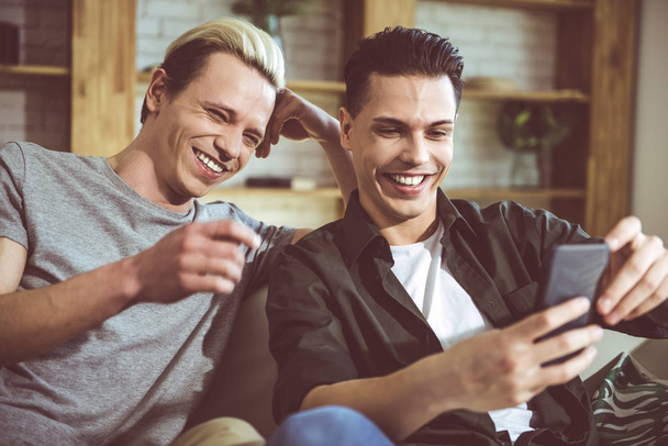 Twee jonge mannen smartphone scherm kijken en lachen - Foto, afbeelding