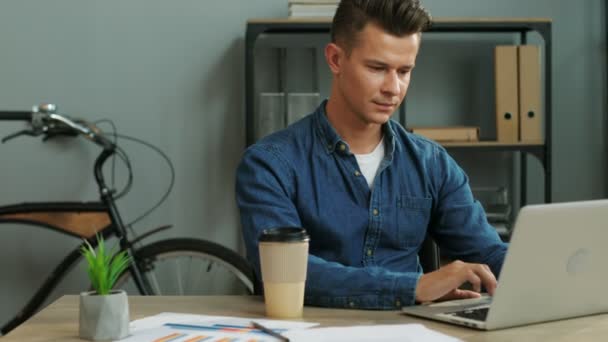 Young business man working in the modern office, using laptop and drinking the coffee. - Materiał filmowy, wideo