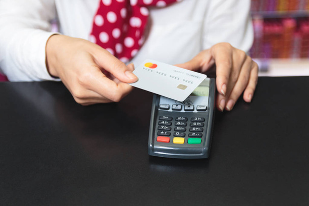 Handen van een vrouwelijke winkelbediende een credit card bedrijf en het maken van betaling draadloos - Foto, afbeelding