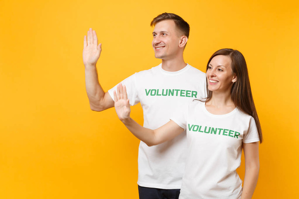 Портрет молодых коллег пара в белой футболке с надписью зеленый заголовок добровольца изолированы на желтом фоне. Добровольная бесплатная работа, помощь, благотворительная благотворительная концепция совместной работы
 - Фото, изображение