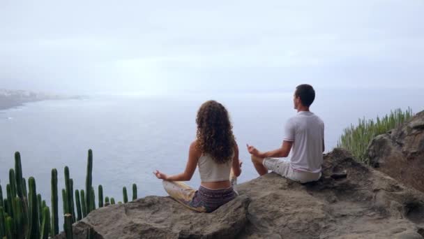 Ένας άνδρας και μια γυναίκα που κάθεται στην κορυφή ενός βουνού που βλέπει στον ωκεανό που κάθεται σε μια πέτρα διαλογισμό στη θέση Lotus. Η θέα από το πίσω μέρος. Κανάριοι Νήσοι - Πλάνα, βίντεο