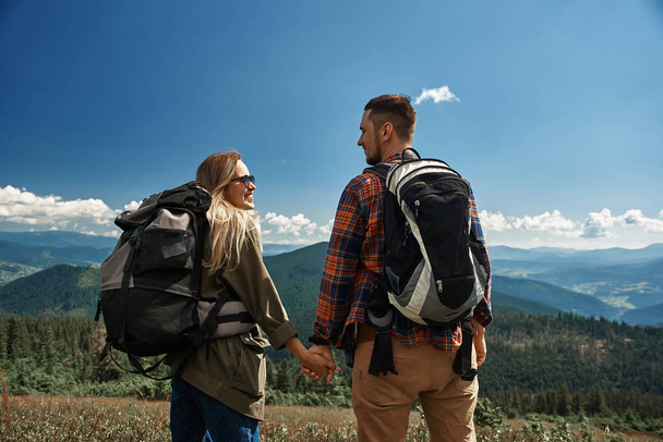 Sonriente hombre y mujer están caminando juntos en las montañas
 - Foto, Imagen