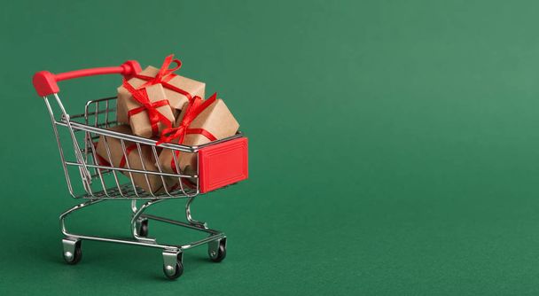 Shopping cart with craft Christmas gifts over green background - Foto, Imagem