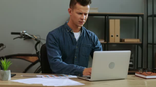 Atractivo hombre de negocios con camisa casual que trabaja en la computadora portátil en la oficina con estilo, sintiendo un dolor de espalda anoying
. - Metraje, vídeo