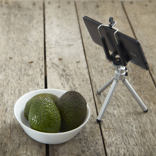 Smartphone-Stativaufnahme mit Avocado auf einem Holztisch, leerer Raum - Foto, Bild