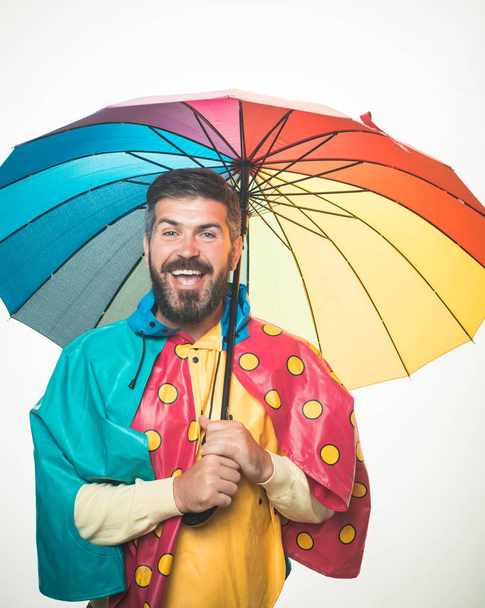 Autumn mood and the weather are warm and sunny and rain is possible. Brutal bearded man with rainbow-colored umbrella isolated on white background. Rain weather. Cloud rain umbrella. Raining concept. - Φωτογραφία, εικόνα