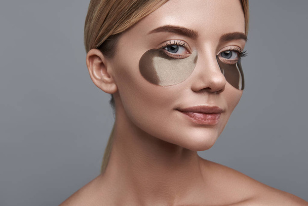 Pretty girl smiling and looking at you while using eye patches - Foto, Imagem