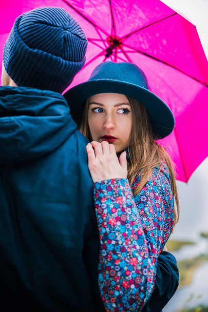 Portrait of young couple who stands to hugs each other with pink umbrella outdoor - Fotó, kép