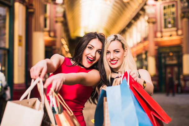 Close-up two joyful pretty women keep shopping bags in hands, outdoors - Foto, afbeelding