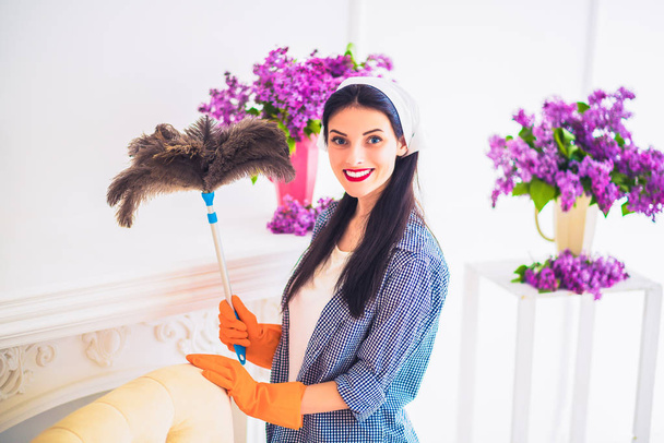 Молодая улыбающаяся домохозяйка вытирает пыль о мебель дома
 - Фото, изображение