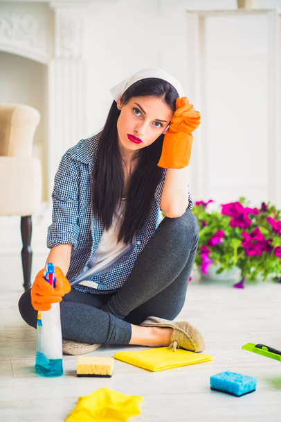 Young weary housewife sits on the floor at home with cleaners for cleaning - 写真・画像