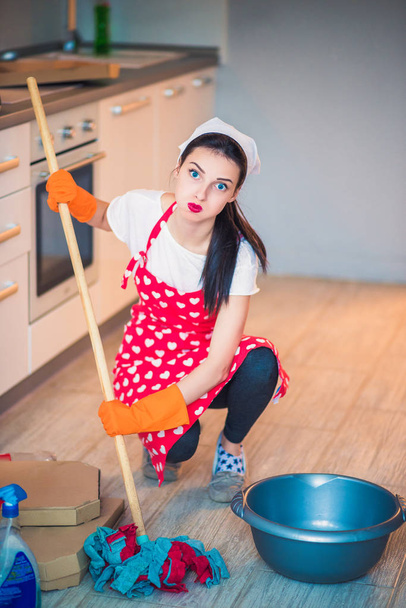 Portrait d'une jeune femme de ménage fatiguée qui s'assoit sur la cuisine et lave le sol
 - Photo, image