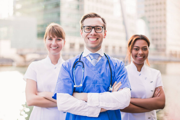 Three happy doctors stand against the background of buildings outdoor - Photo, Image