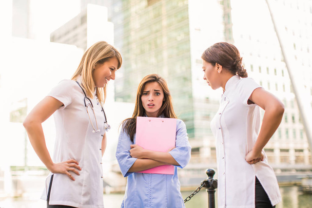 Three young nurses stand together and discuss their problems, one of them is very sad, outdoors - Zdjęcie, obraz