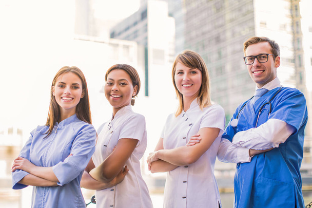 Cuatro trabajadores médicos felices de pie de brazos cruzados, al aire libre
 - Foto, Imagen