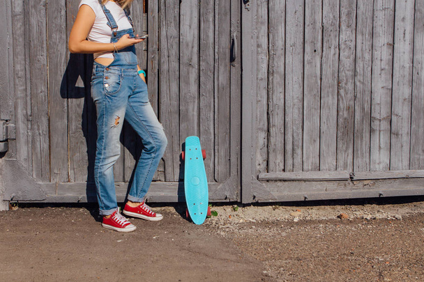 Close up pés de uma menina em tênis vermelho e azul penny skate bordo com rodas cor de rosa em pé ao lado da parede. Cena urbana, vida na cidade. Desporto, fitness lifestyle
. - Foto, Imagem