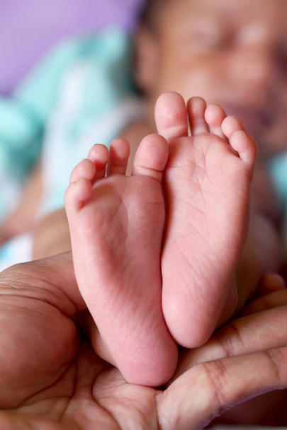Κοντινό πλάνο του tiny πόδι νεογέννητο μωρό στα χέρια του γονέα - Φωτογραφία, εικόνα
