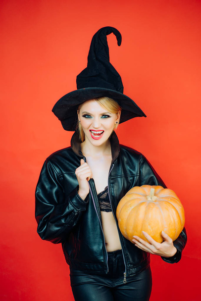 Emotional young women in halloween costumes on party over red background with pumpkin. Witch posing with Pumpkin. - Fotó, kép