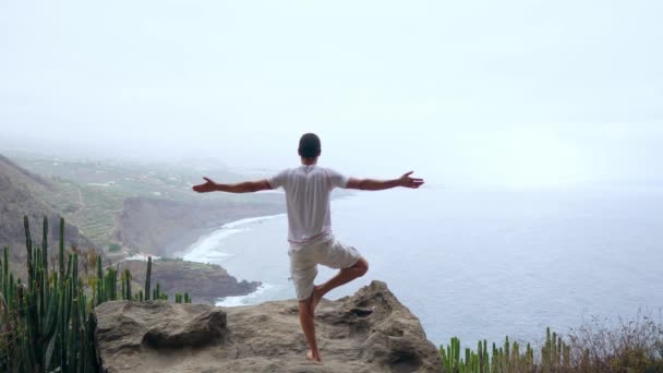 Fit młody człowiek uprawia jogę pozdrowienie słońca w góry dla ocean. Młody człowiek korzystających medytacji i jogi. fitness, sport, ludzie i lifestyle concept - młody człowiek wykonywanie ćwiczeń jogi. - Materiał filmowy, wideo