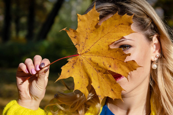 Una joven, hermosa, rubia mujer caminando por el parque de otoño y regocijarse en hojas de árboles de colores
. - Foto, Imagen