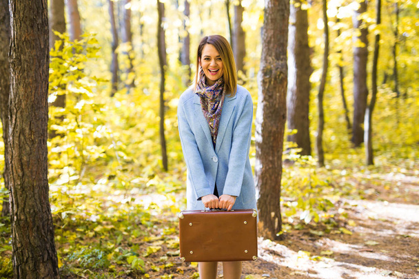 Season, nature and people concept - Woman in autumn park standing with suitcase - Фото, зображення