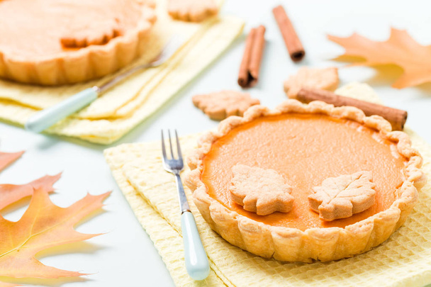 Pumpkin pie with cinnamon and cookies on yellow napkins on pastel blue background with autumn yellow leaves - top view close up photography of seasonal american traditional sweet baked food. - Photo, Image