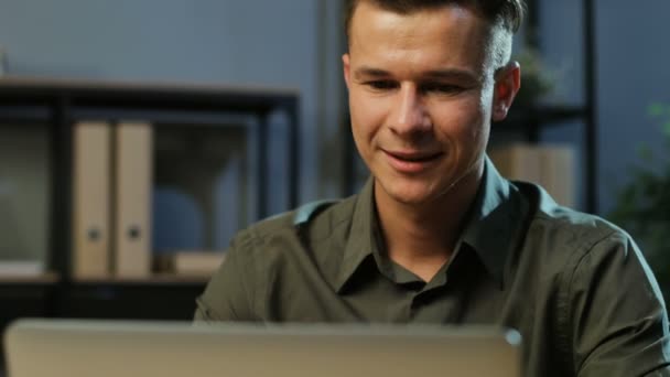 Close up portrait of happy young business man in khaki shirt working on the laptop in the stylish office at the evening time. - Imágenes, Vídeo