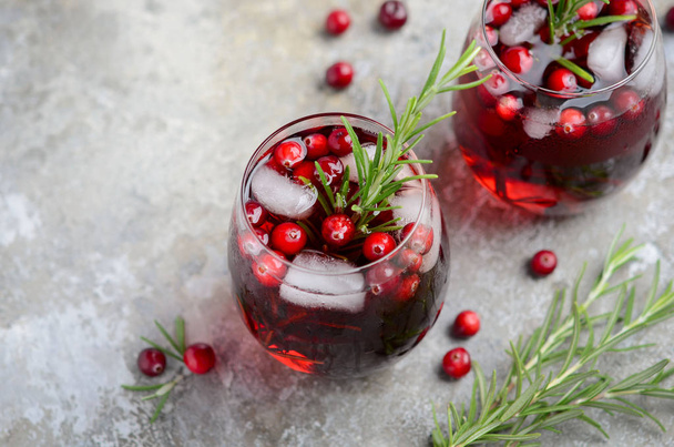 Cold refreshing drink with cranberries and rosemary on a gray concrete background - 写真・画像