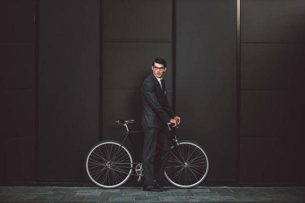 Young handsome man with business suit driving bycicle - Corporate businessman portrait, concepts about business, mobility and lifestyle - Fotó, kép
