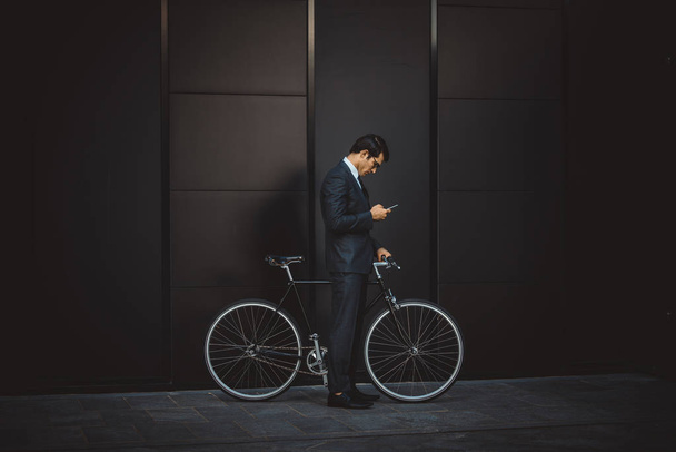 Young handsome man with business suit driving bycicle - Corporate businessman portrait, concepts about business, mobility and lifestyle - Zdjęcie, obraz