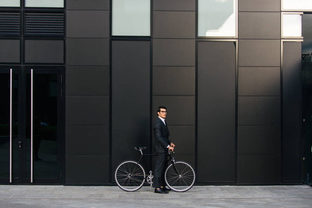 Joven hombre guapo con traje de negocios bicicleta de conducción - Retrato de hombre de negocios corporativo, conceptos sobre negocios, movilidad y estilo de vida
 - Foto, Imagen