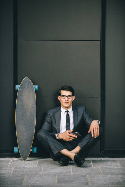 Young handsome man with business suit riding on a longboard - Corporate businessman portrait, concepts about business, mobility and lifestyle - Photo, image