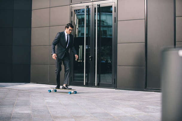 Young handsome man with business suit riding on a longboard - Corporate businessman portrait, concepts about business, mobility and lifestyle - Photo, image