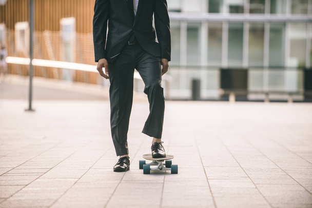 Young handsome man with business suit riding on a longboard - Corporate businessman portrait, concepts about business, mobility and lifestyle - Photo, Image