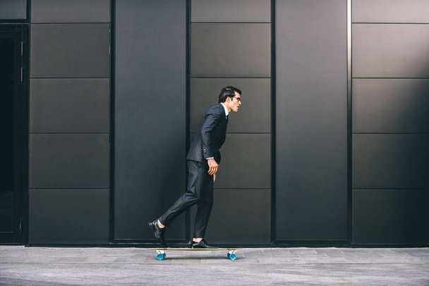 Young handsome man with business suit riding on a longboard - Corporate businessman portrait, concepts about business, mobility and lifestyle - Zdjęcie, obraz