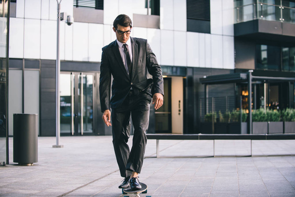Young handsome man with business suit riding on a longboard - Corporate businessman portrait, concepts about business, mobility and lifestyle - Фото, зображення