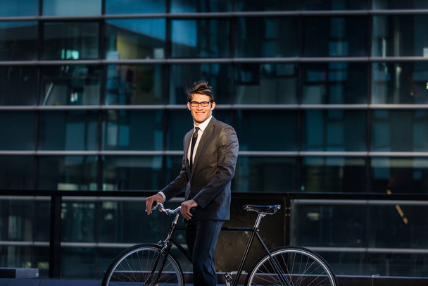 Young handsome man with business suit driving bycicle - Corporate businessman portrait, concepts about business, mobility and lifestyle - 写真・画像