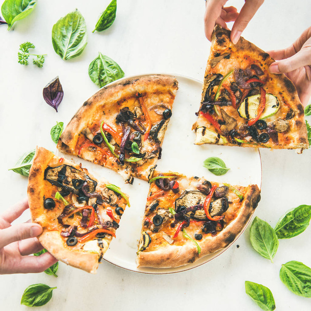Summer dinner or lunch. People's hands taking freshly baked Italian vegetarian pizza with vegetables and fresh basil over white marble table - Photo, image