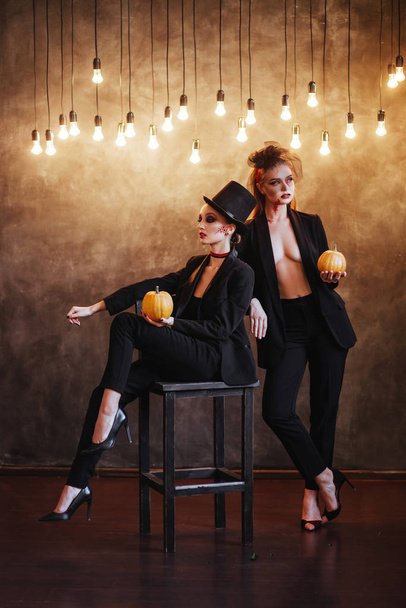 Two happy young women in black witch halloween costumes on dark background - Fotoğraf, Görsel