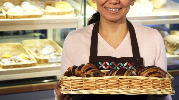 Bijgesneden shot van een vrolijke vrouwelijke Bakker poseren met een mand vol croissants - Foto, afbeelding