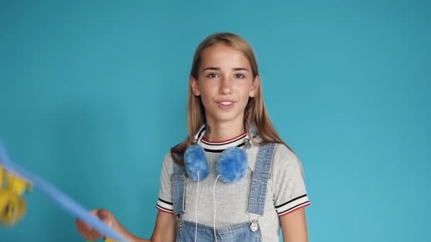 Portrait of a teen girl with skateboard on her shoulder on blue background. Free time of teenagers. Leisure and sport activity. Happy pretty teenage girl holding skateboard on her shoulders and - Séquence, vidéo