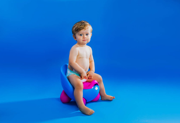 Cute little boy sits on pot against blue background - Фото, зображення
