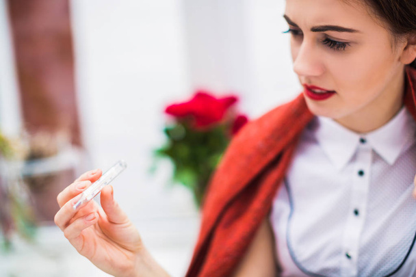 Close-up photo of sick woman who keeps thermometer in hand and looks at it indoor - Photo, Image