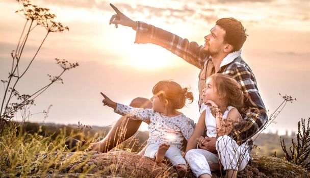 Happy loving family, dad playing with two little cute daughters at sunset sitting on a high beautiful mountain, the concept of family relationships and friendship - Photo, Image