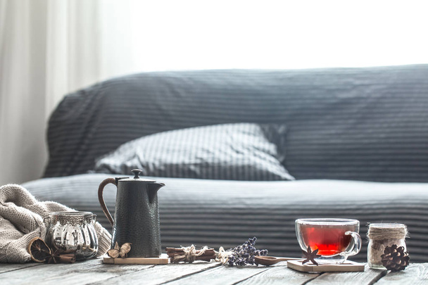 natura morta accogliente soggiorno con elementi di arredamento per la casa e una tazza di tè con una teiera su un tavolo di legno
 - Foto, immagini