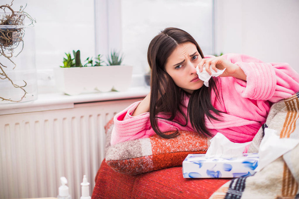 Young sick woman lies on bed at home wipes nose of napkin - Foto, Bild