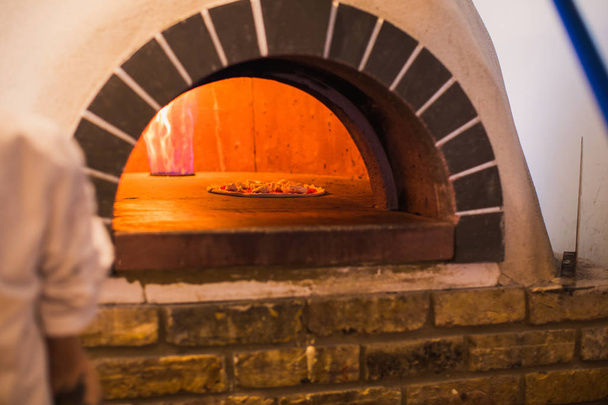 Close-up van de pizza is gebakken in de oven op brand in de keuken - Foto, afbeelding