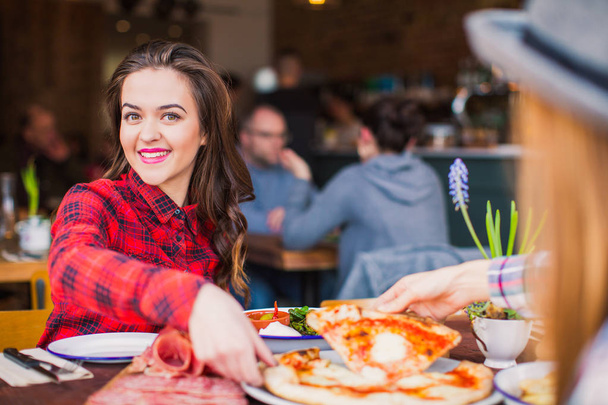 Two cheerful women sit at the table and take slices of pizza, in restaurant - Foto, Bild
