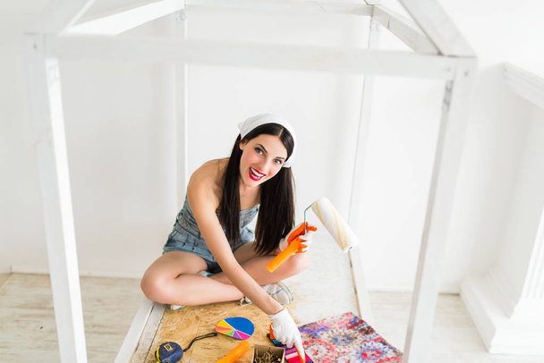 The young happy brunette female sits on crib on which are tools for repair - Photo, image