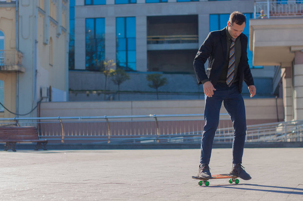 businessman in a business suit stands in the background of the building holds a skateboard - Photo, Image